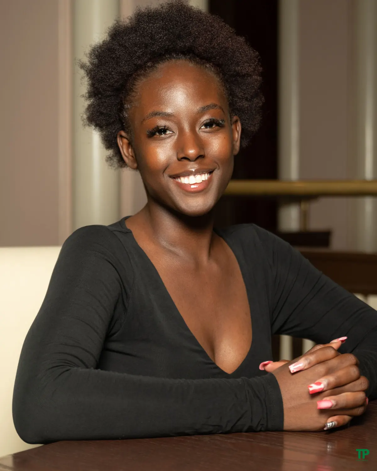 Smiling woman with natural hair seated at a wooden table in warm indoor light