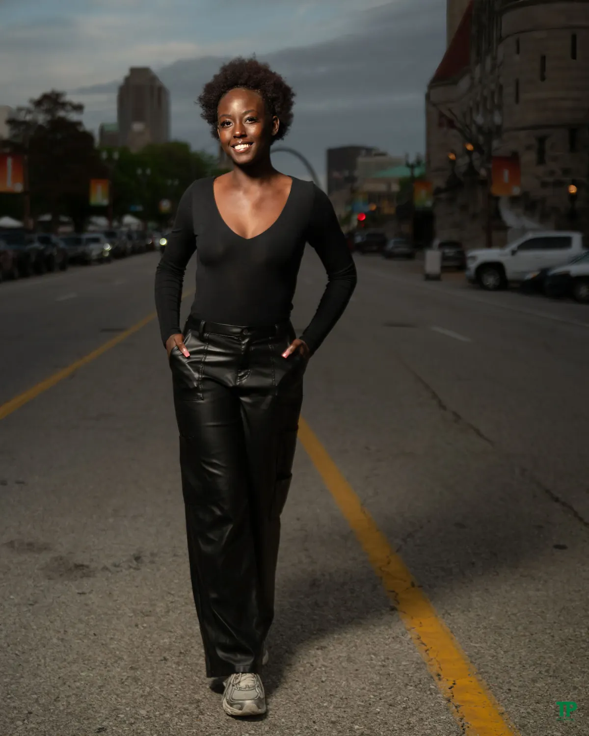 Smiling woman in a black top and leather trousers standing on a city street
