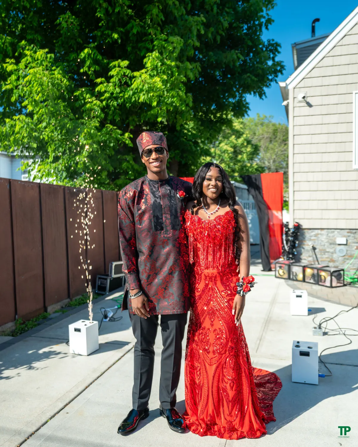 Smiling prom pair in coordinated red and black formalwear posing at an outdoor send-off