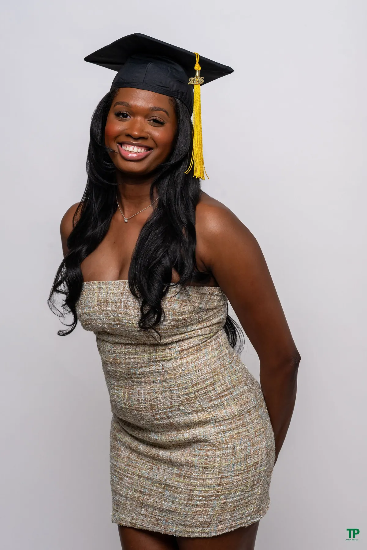 Smiling graduate in a metallic strapless dress and black graduation cap against a white studio background