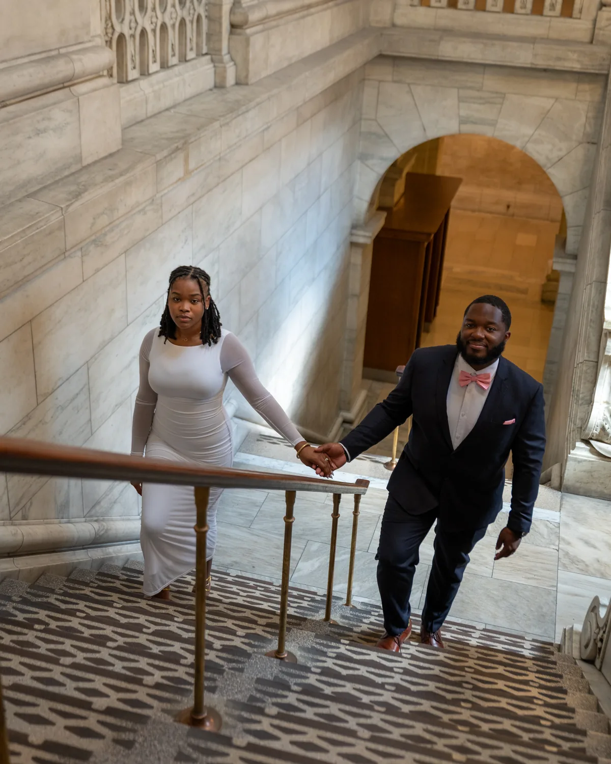 Couple holding hands while walking up a grand staircase