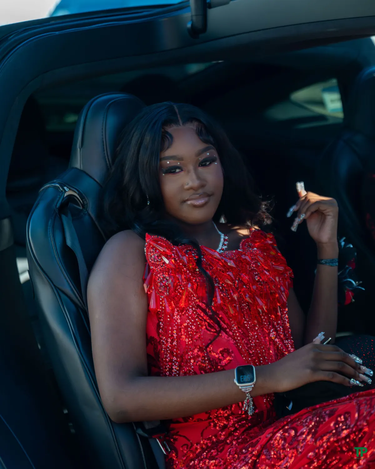 Prom attendee in a red beaded gown seated inside a car