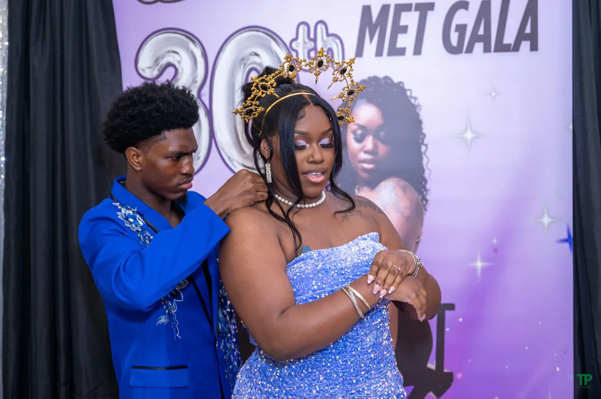 Birthday guest of honor in a blue sequined gown as a guest adjusts her necklace