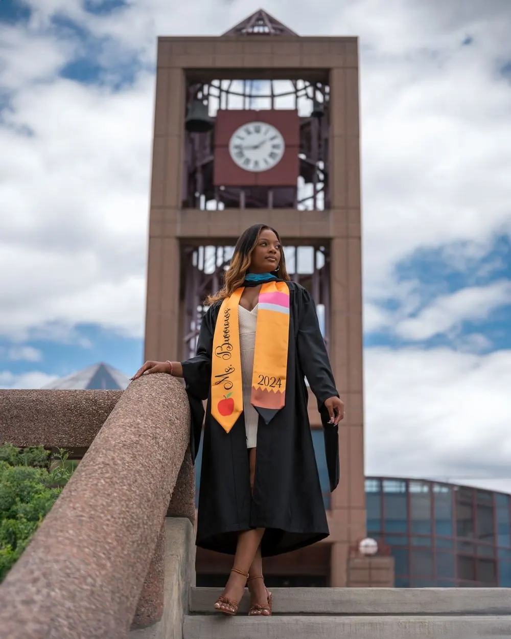 Graduate in a black gown and colorful stole before a clock tower