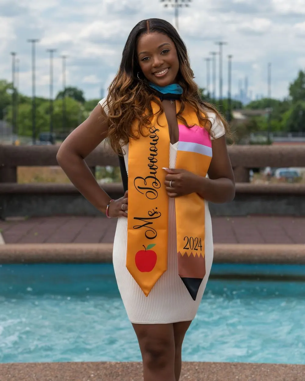 Graduate wearing a yellow stole posed near a fountain