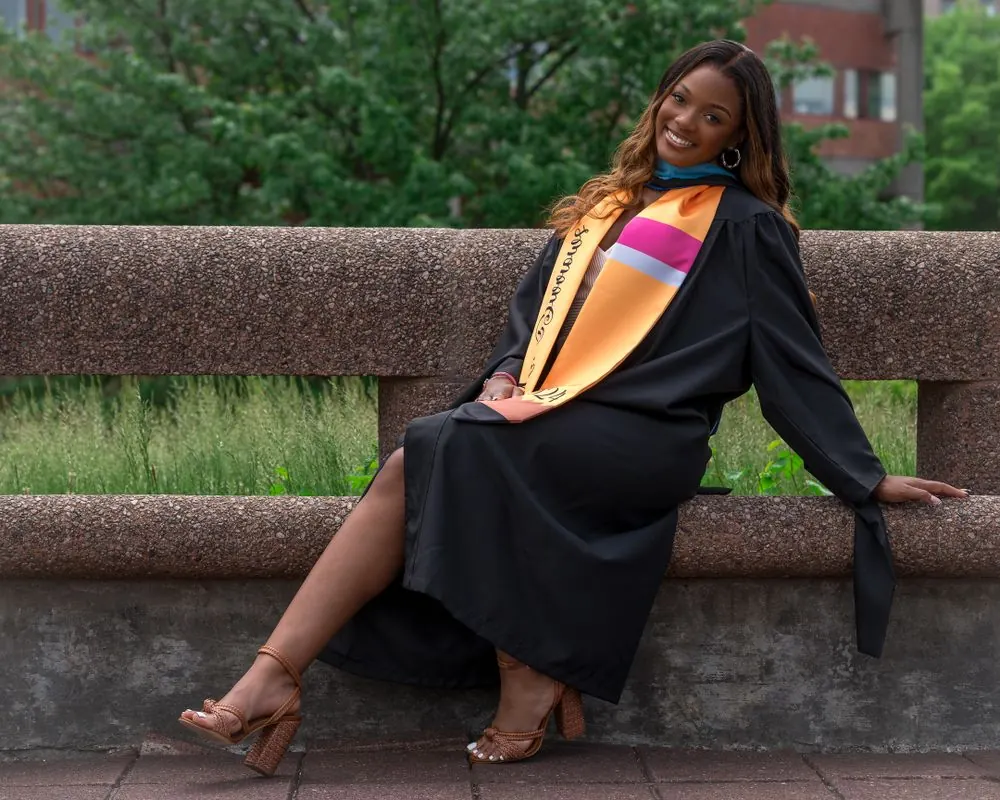 Graduate in a black gown seated on a stone bench