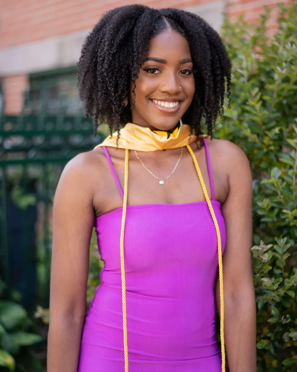Smiling graduate in a purple dress and gold cords outdoors