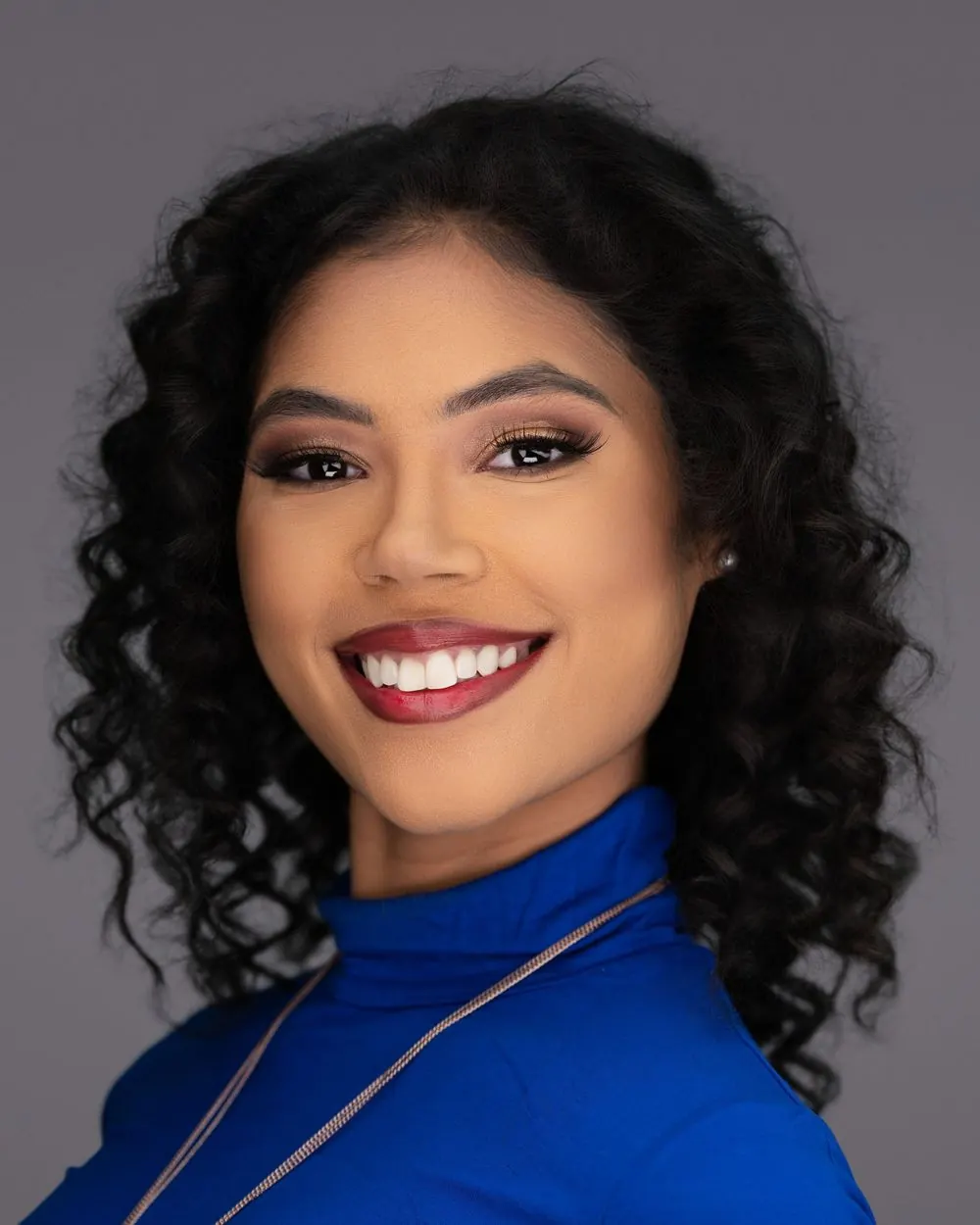 Smiling woman in a blue top photographed against a dark studio background