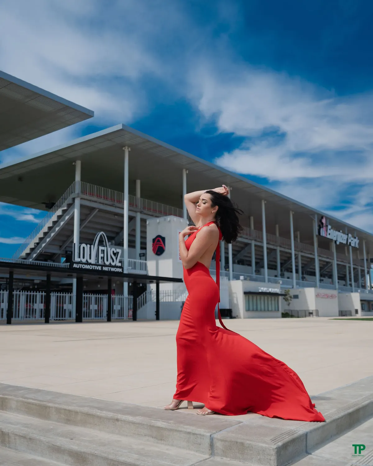 Woman in a flowing red gown posing beside modern architecture under a blue sky