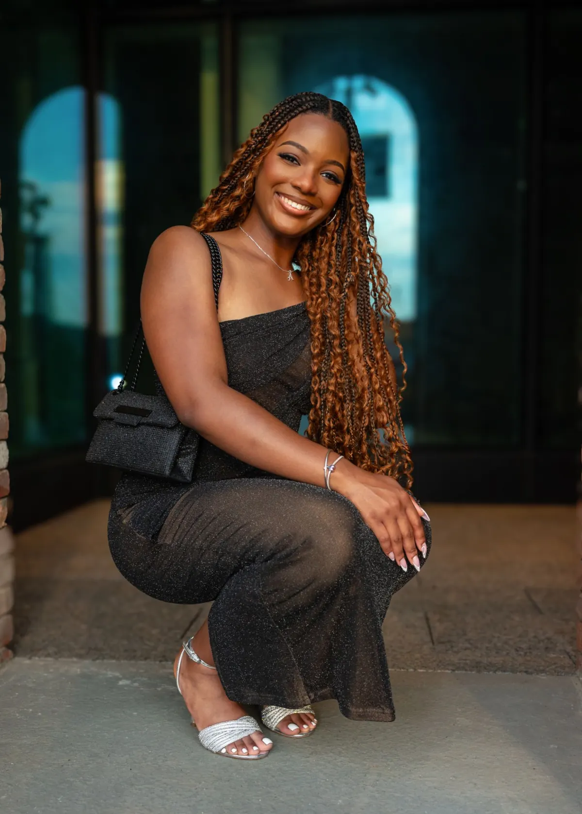 Smiling woman with long braids seated in a black dress
