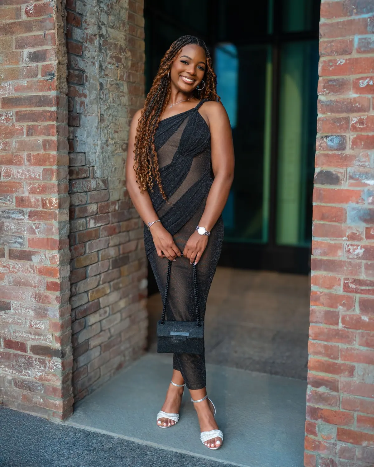Smiling woman in a black dress standing between brick walls