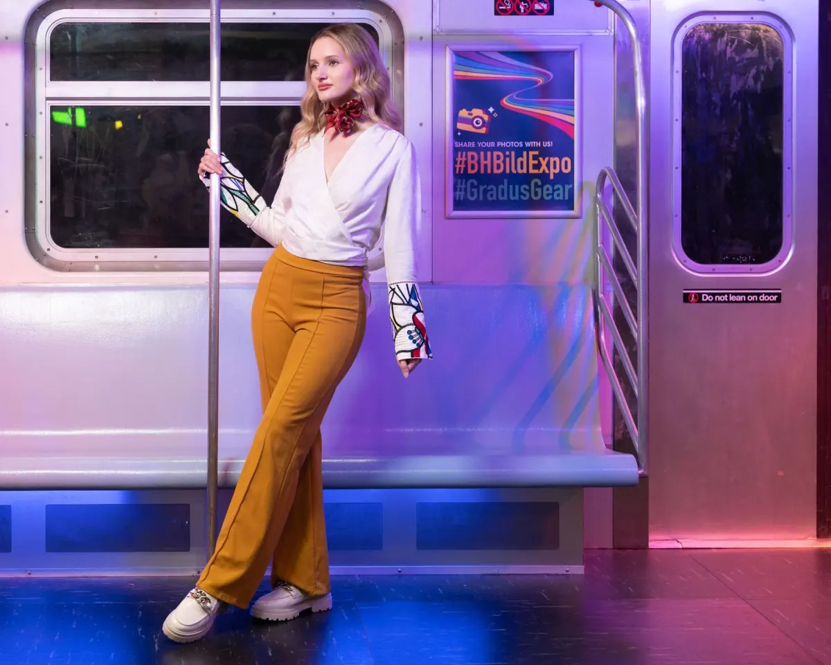 Woman in a white blouse leaning against a pole in a train car