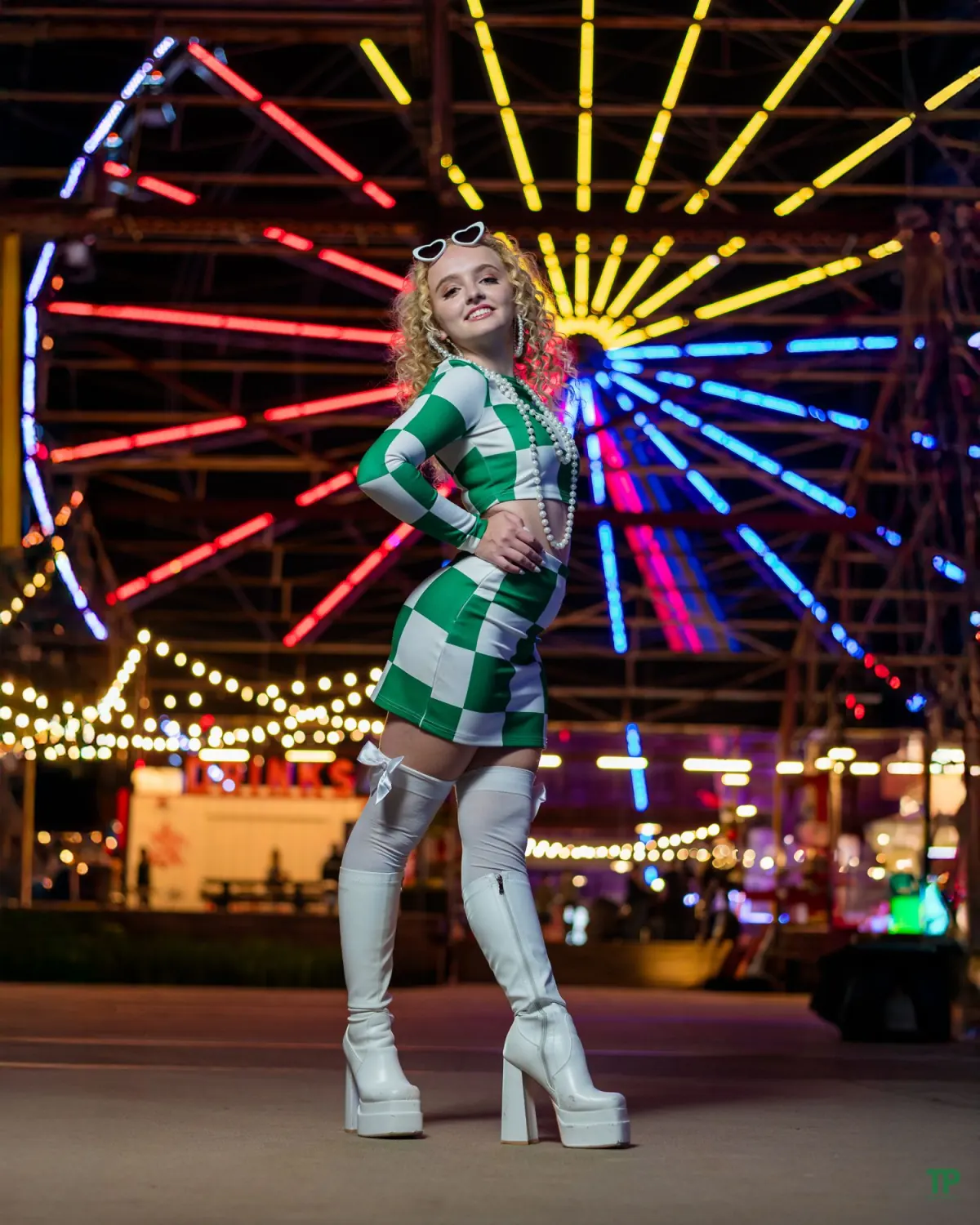 Woman in a green checked dress posed before colorful carnival lights