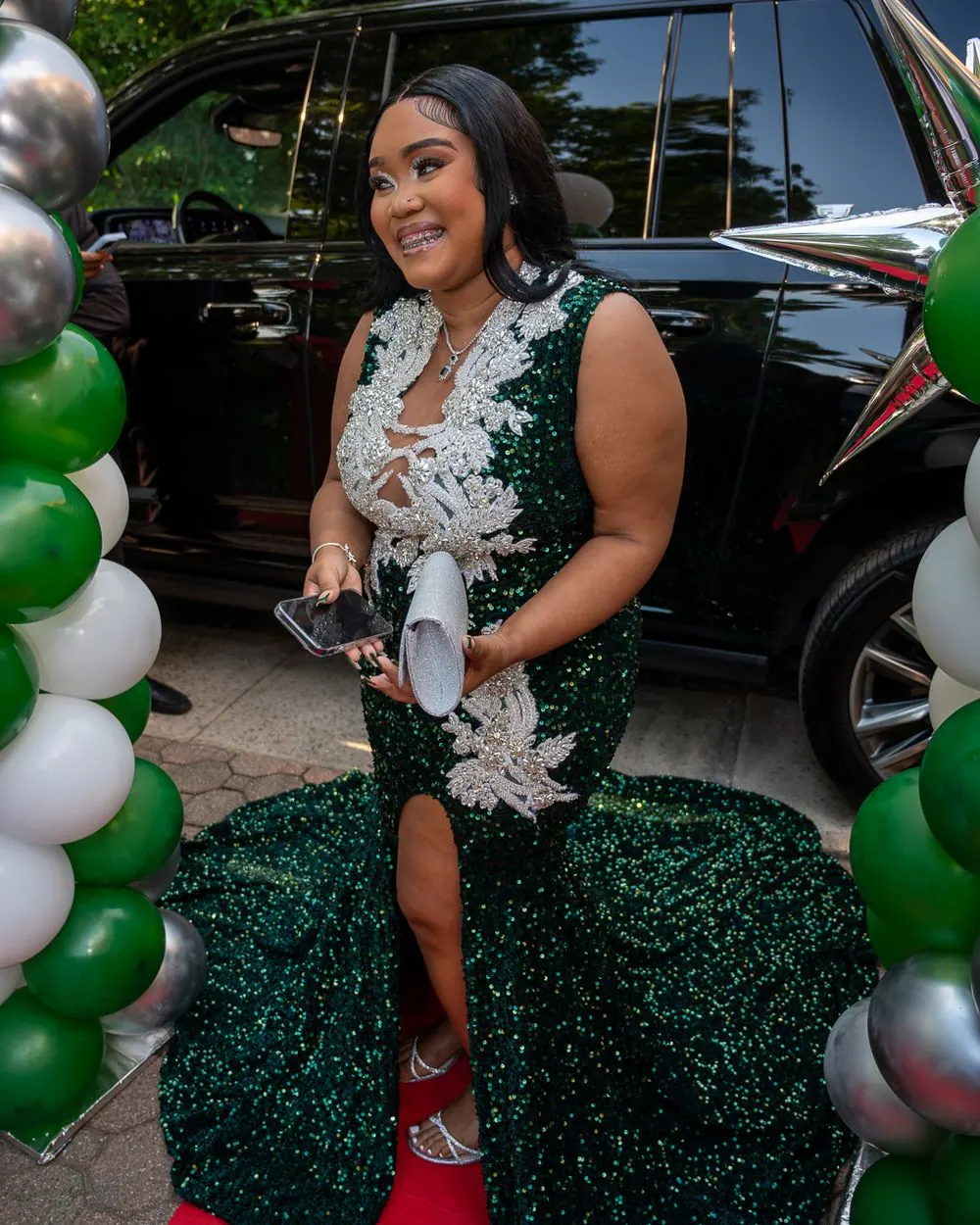 Prom attendee in a green sequined dress arriving beside a car and balloons