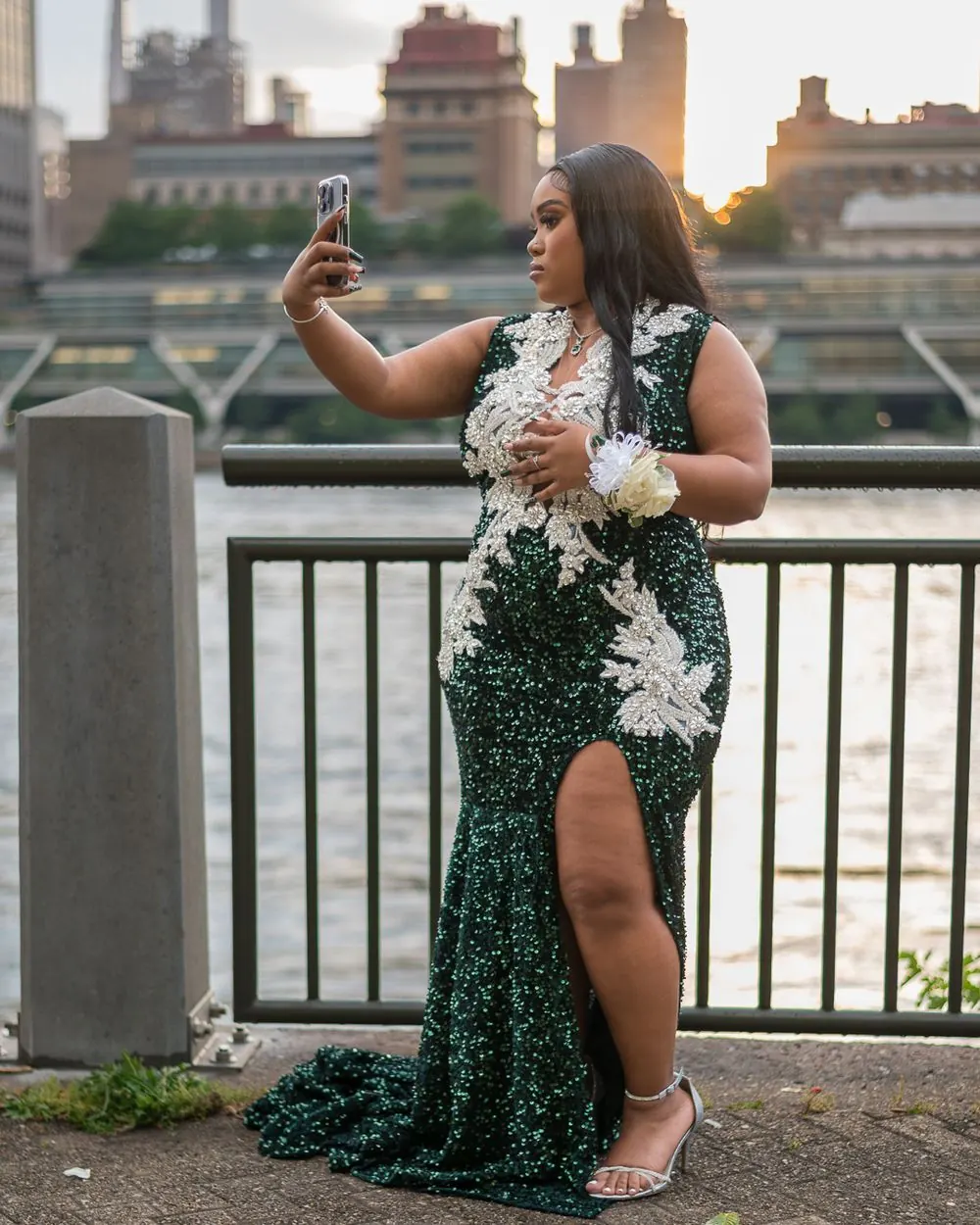 Prom attendee in a green sequined dress by the waterfront at sunset