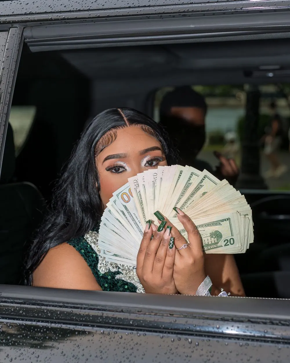 Prom attendee holding a fan of bills through a car window