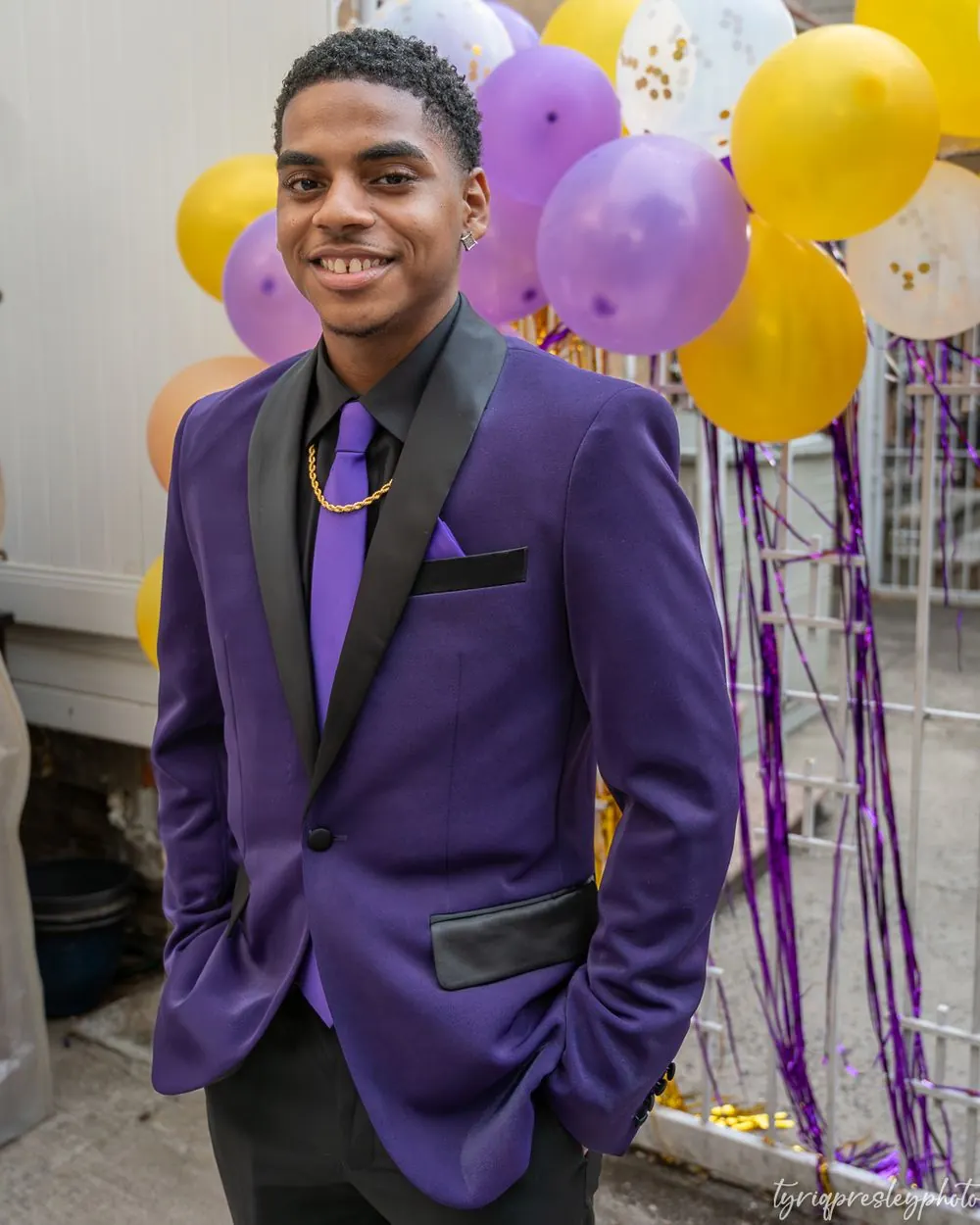 Young man in a purple suit smiling in front of balloons